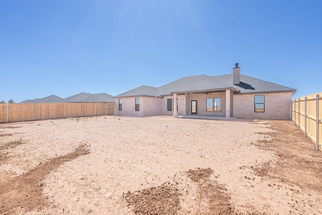 back of property with a patio area, a fenced backyard, brick siding, and a chimney