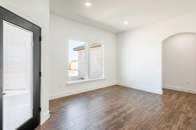 empty room featuring arched walkways, dark wood-style flooring, baseboards, and recessed lighting