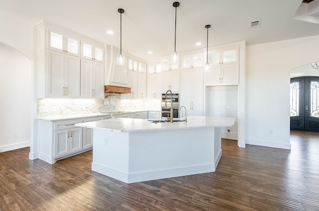 kitchen featuring arched walkways, visible vents, glass insert cabinets, white cabinets, and an island with sink