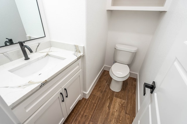 half bath featuring toilet, vanity, baseboards, and wood finished floors