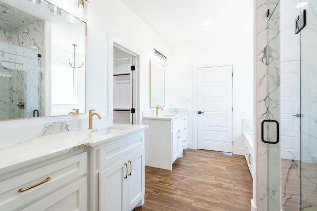 bathroom with a sink, wood finished floors, two vanities, and a marble finish shower