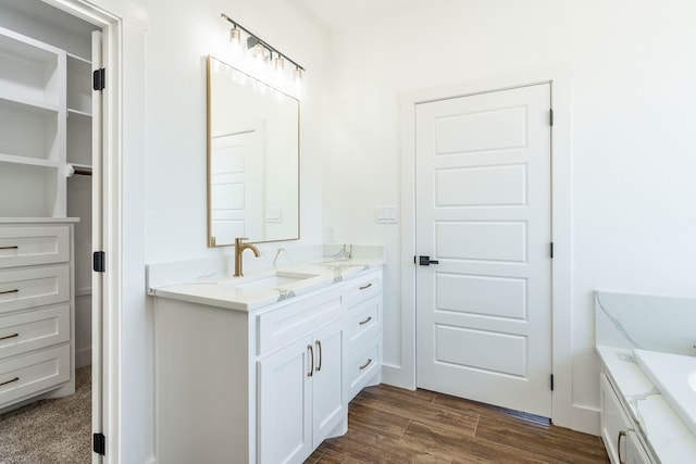 full bath with a washtub, a walk in closet, vanity, and wood finished floors