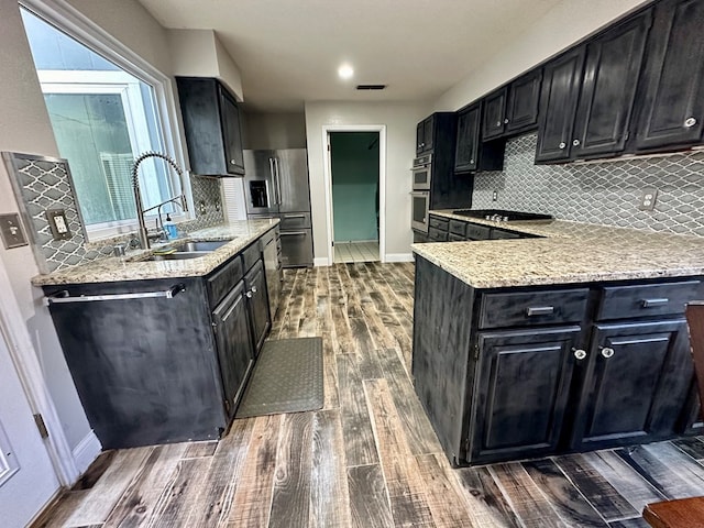 kitchen with light stone countertops, tasteful backsplash, stainless steel appliances, dark wood-type flooring, and sink