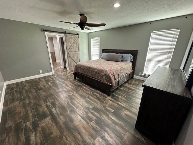 bedroom with a barn door, ceiling fan, dark hardwood / wood-style flooring, and a textured ceiling