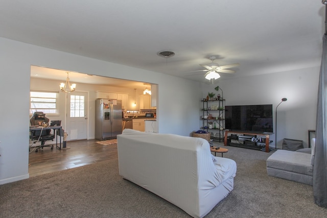 carpeted living room featuring wood finished floors, visible vents, and ceiling fan with notable chandelier