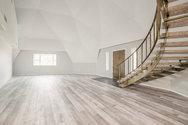 unfurnished living room with a towering ceiling, baseboards, stairway, and wood finished floors