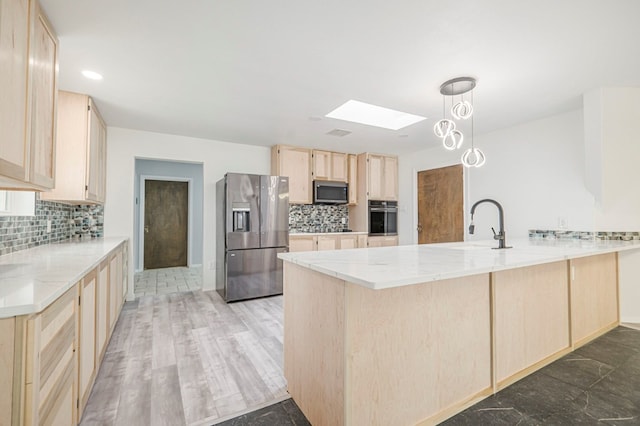 kitchen with light stone counters, a skylight, light brown cabinetry, appliances with stainless steel finishes, and a peninsula