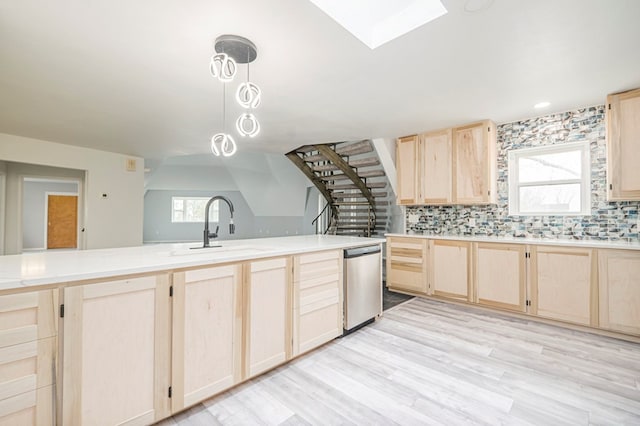 kitchen featuring light brown cabinets, a skylight, a sink, light countertops, and stainless steel dishwasher