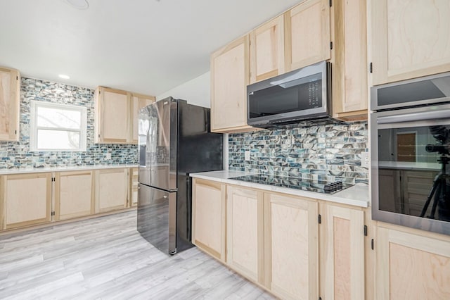 kitchen with appliances with stainless steel finishes, light brown cabinets, light wood finished floors, and decorative backsplash