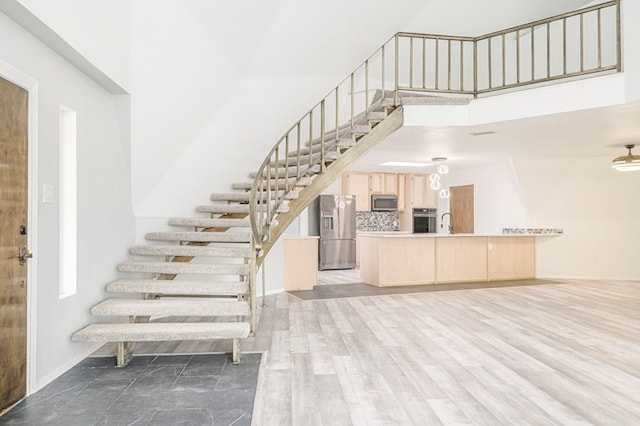 staircase featuring a towering ceiling, baseboards, and wood finished floors