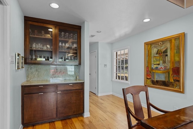 bar featuring light wood finished floors, baseboards, a bar, backsplash, and recessed lighting