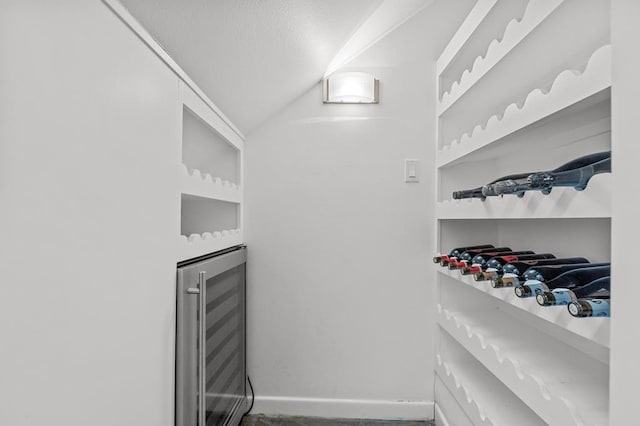 wine area featuring beverage cooler, a textured ceiling, lofted ceiling, and baseboards