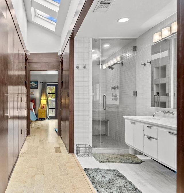 ensuite bathroom featuring wood finished floors, vanity, visible vents, a shower stall, and lofted ceiling with skylight