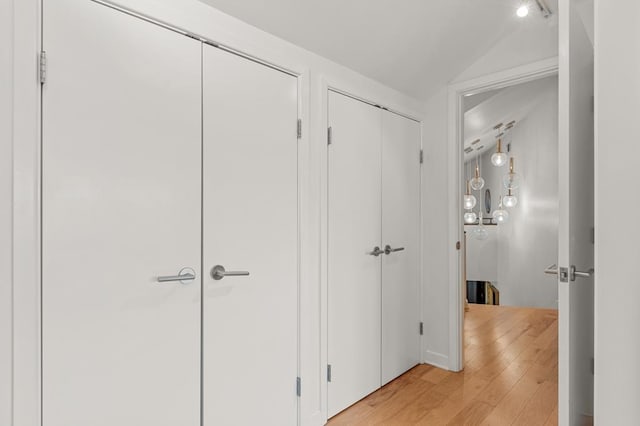 corridor with light wood-style floors and vaulted ceiling