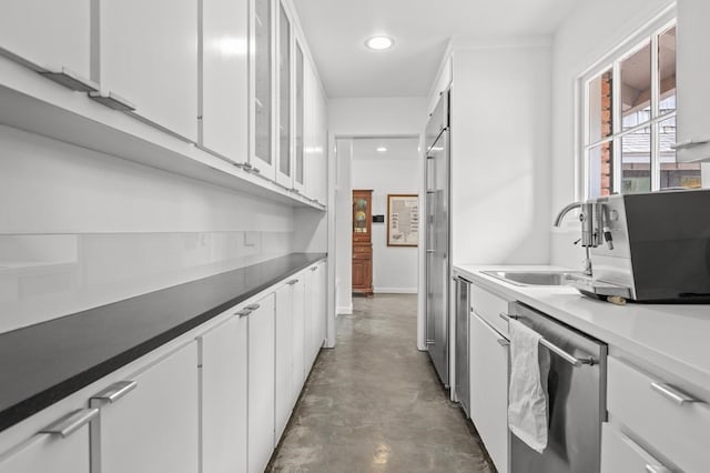 kitchen featuring stainless steel dishwasher, a sink, finished concrete floors, and white cabinets