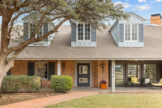 view of front of property with a shingled roof, brick siding, and a chimney