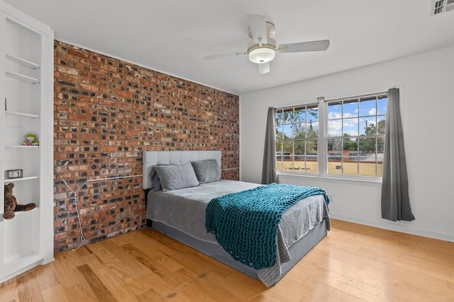 bedroom with ceiling fan, light wood-style flooring, brick wall, visible vents, and baseboards