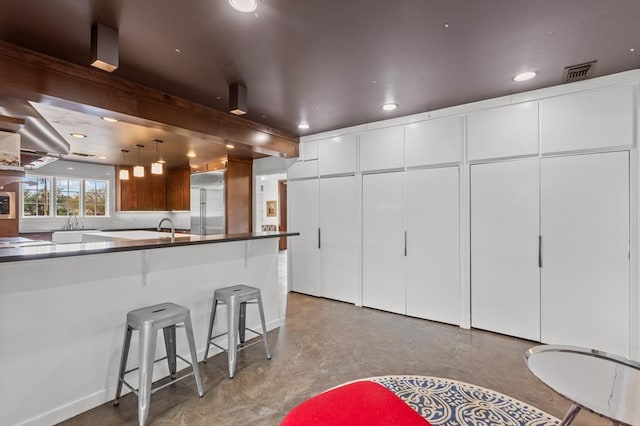 kitchen featuring a breakfast bar, pendant lighting, dark countertops, visible vents, and built in refrigerator