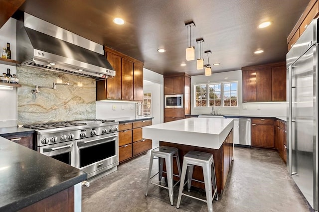 kitchen with wall chimney exhaust hood, built in appliances, a sink, concrete floors, and backsplash