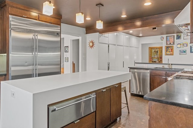 kitchen with a warming drawer, dark countertops, appliances with stainless steel finishes, a sink, and concrete floors