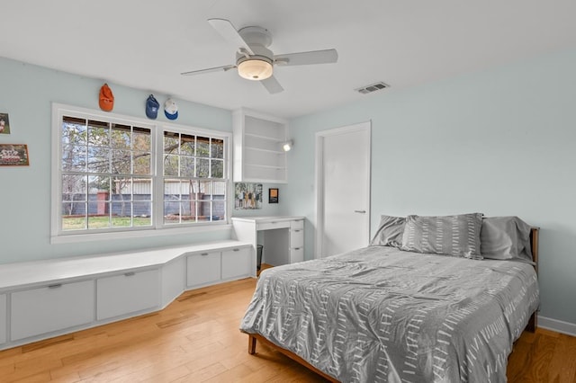 bedroom featuring light wood finished floors, built in study area, visible vents, and a ceiling fan