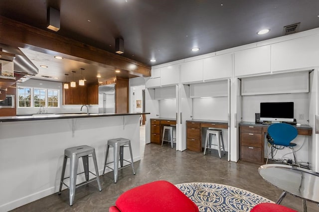 kitchen featuring a breakfast bar, finished concrete flooring, recessed lighting, visible vents, and white cabinets