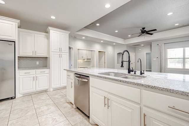 kitchen with a tray ceiling, light stone countertops, stainless steel appliances, and a sink