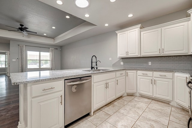 kitchen featuring a peninsula, a tray ceiling, a sink, ceiling fan, and dishwasher