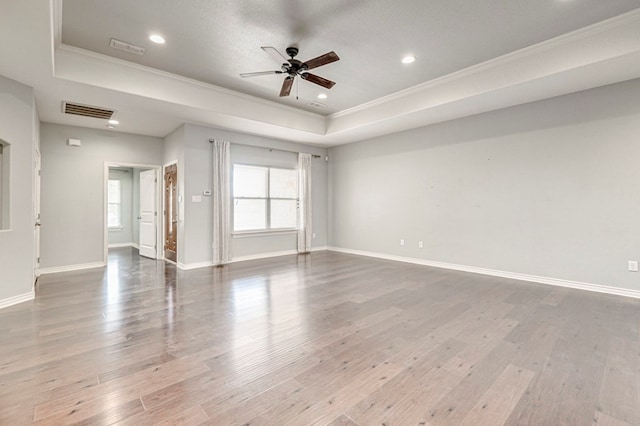 empty room featuring a ceiling fan, crown molding, wood finished floors, a tray ceiling, and visible vents