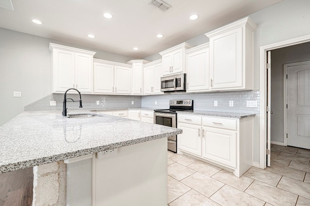 kitchen with a sink, white cabinets, a peninsula, appliances with stainless steel finishes, and visible vents