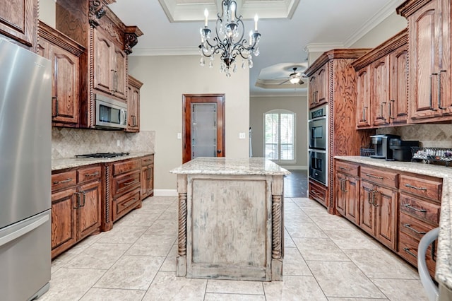 kitchen with a raised ceiling, ceiling fan with notable chandelier, a center island, stainless steel appliances, and ornamental molding