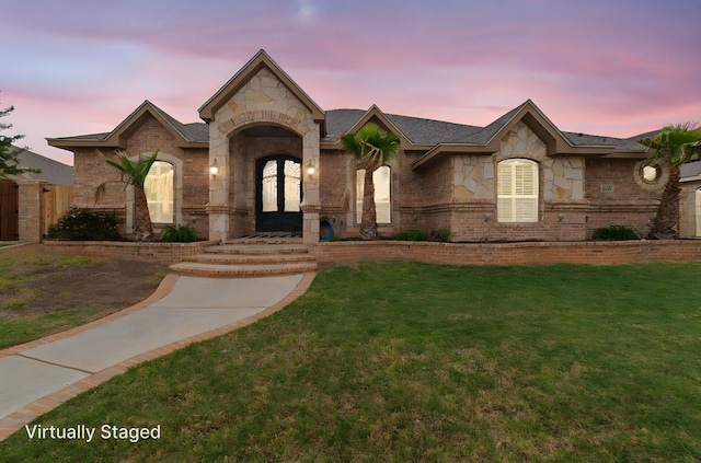 french country style house featuring a lawn, brick siding, french doors, and stone siding
