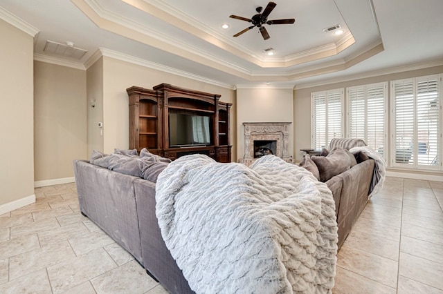 living room featuring ceiling fan, baseboards, a tray ceiling, visible vents, and ornamental molding