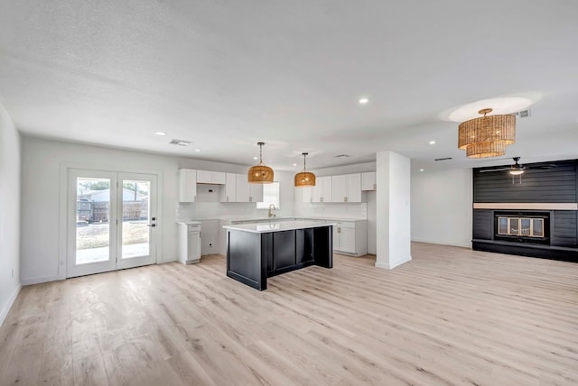 kitchen with light hardwood / wood-style flooring, white cabinetry, hanging light fixtures, a large fireplace, and a kitchen island