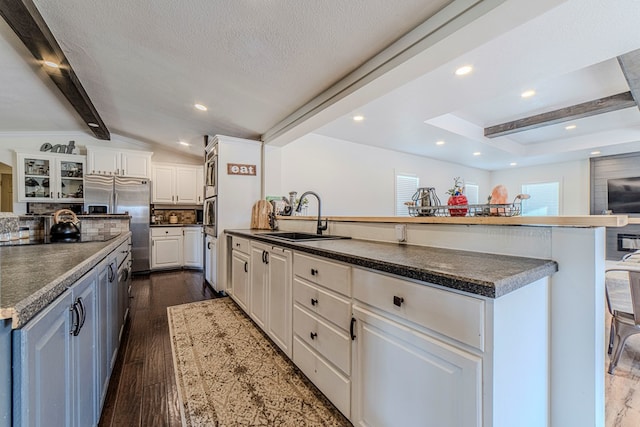 kitchen with sink, dark wood-type flooring, lofted ceiling with beams, a breakfast bar area, and white cabinets