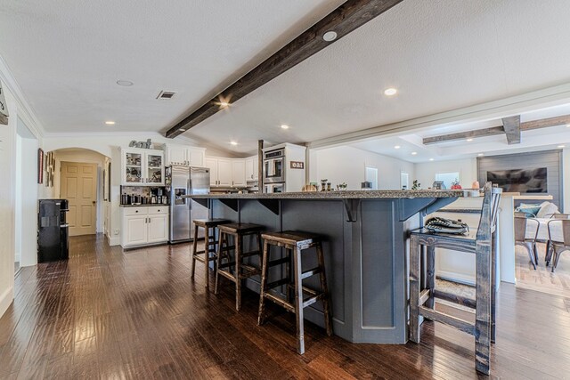 kitchen featuring dark wood-type flooring, stainless steel appliances, white cabinetry, and a breakfast bar area