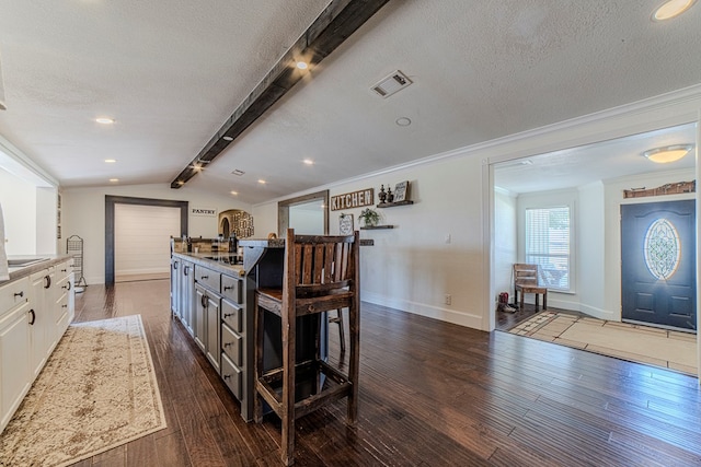 kitchen featuring white cabinets, vaulted ceiling with beams, dark hardwood / wood-style floors, ornamental molding, and a textured ceiling