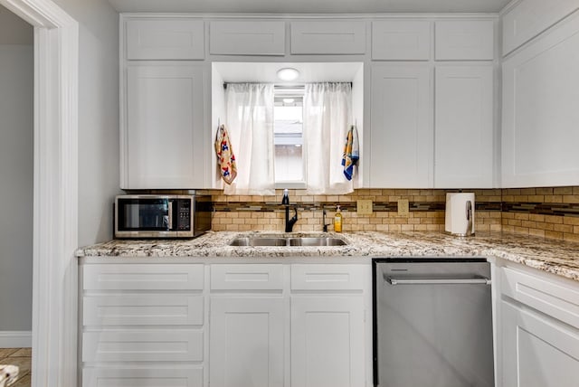 kitchen with white cabinets, light stone counters, appliances with stainless steel finishes, a sink, and tasteful backsplash