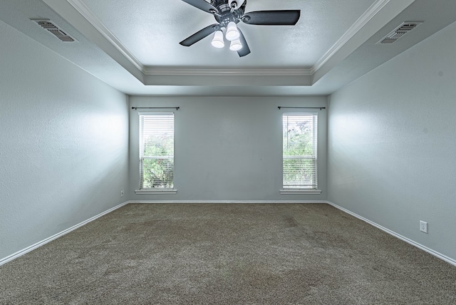 carpeted empty room with ornamental molding, a ceiling fan, a tray ceiling, and visible vents