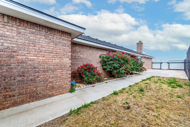 view of home's exterior with brick siding, fence, and a chimney