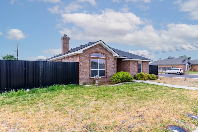 ranch-style home featuring brick siding, fence, a chimney, and a front yard