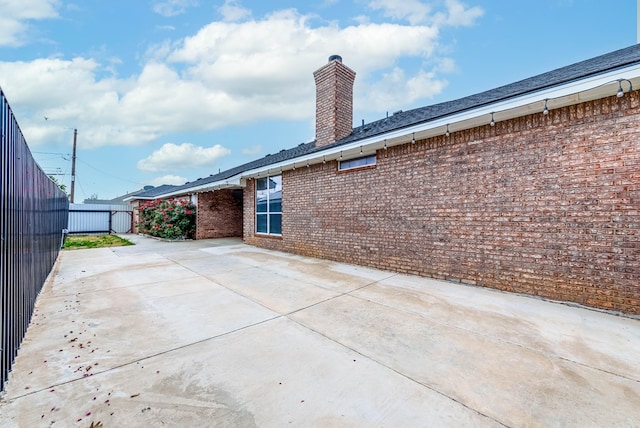 rear view of house featuring brick siding, fence, a chimney, and a patio area