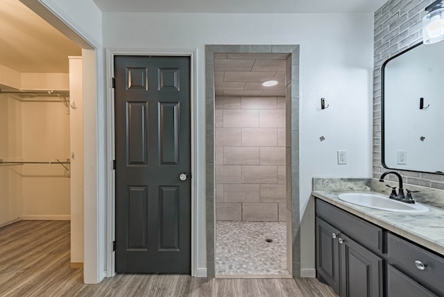 full bathroom featuring wood finished floors, vanity, baseboards, a spacious closet, and tiled shower