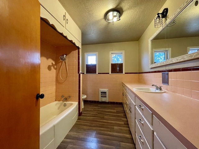 2508 31st St, Snyder, TX 79549 - full bathroom with toilet, heating unit, a textured ceiling, tile walls, and hardwood / wood-style floors