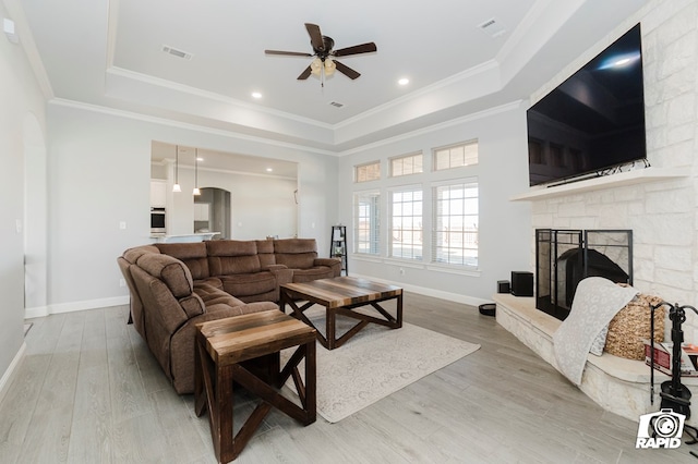 living room with ceiling fan, light wood-type flooring, a fireplace, and a tray ceiling