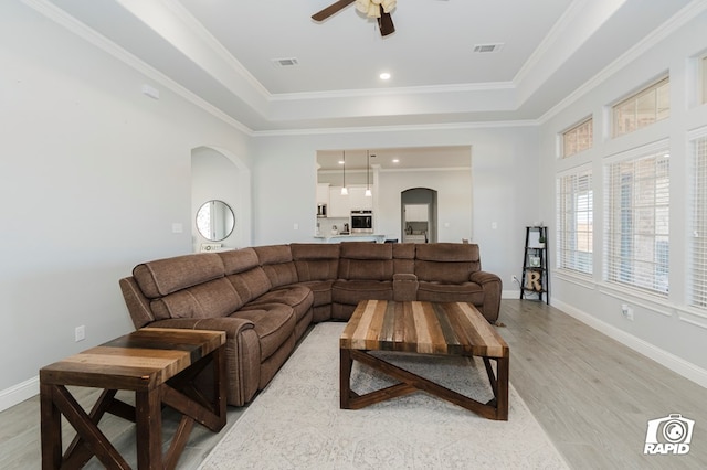 living room with ceiling fan, a raised ceiling, crown molding, and light hardwood / wood-style flooring