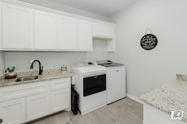 clothes washing area featuring washing machine and dryer, sink, cabinets, and light wood-type flooring