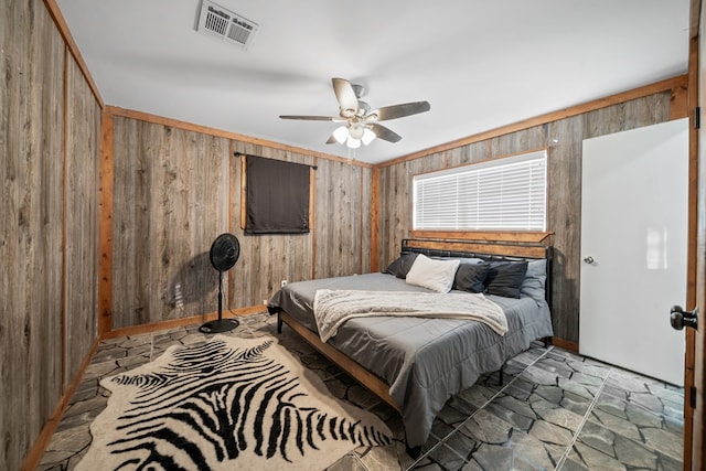 bedroom with visible vents, wooden walls, ceiling fan, ornamental molding, and stone finish floor