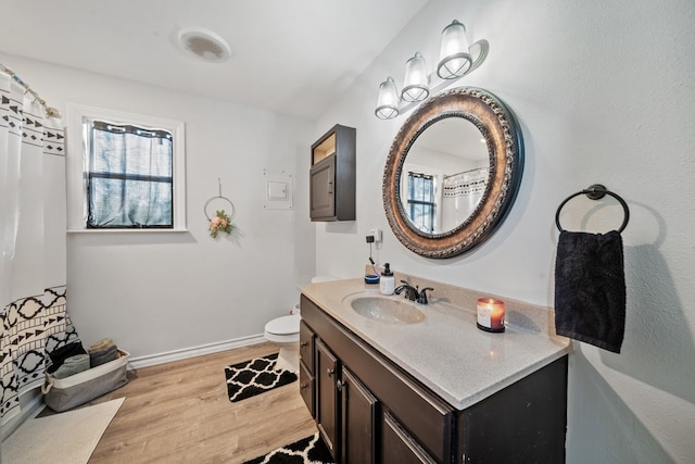 bathroom with vanity, toilet, wood finished floors, and baseboards