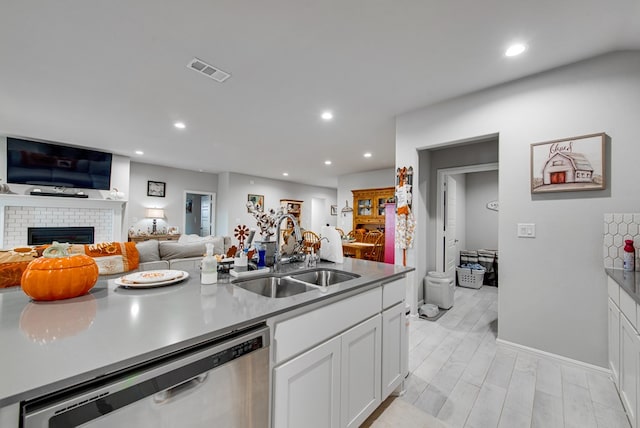 kitchen featuring light wood-type flooring, white cabinets, a fireplace, sink, and dishwasher